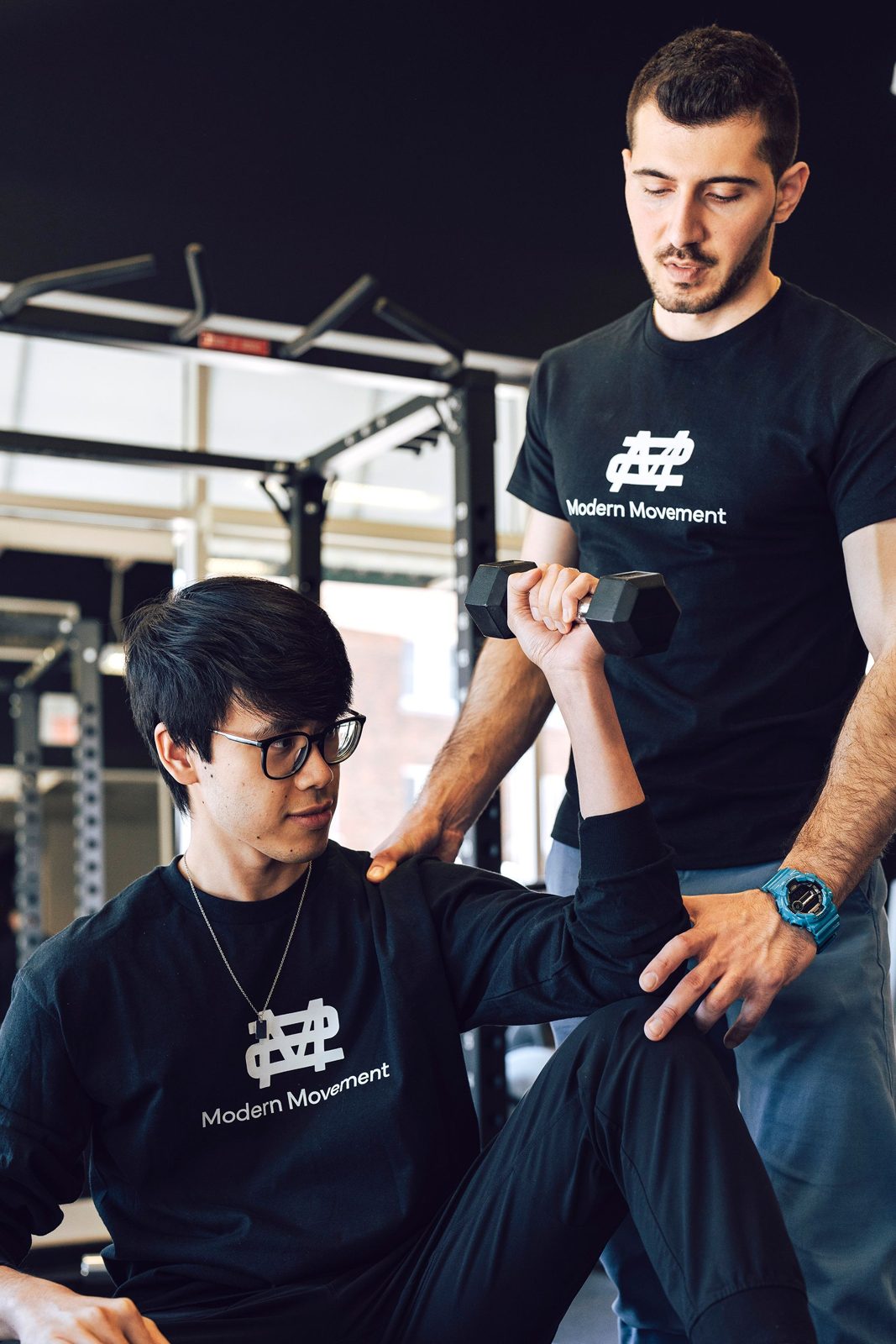 Physiotherapist guiding a seated patient through a dumbbell shoulder exercise